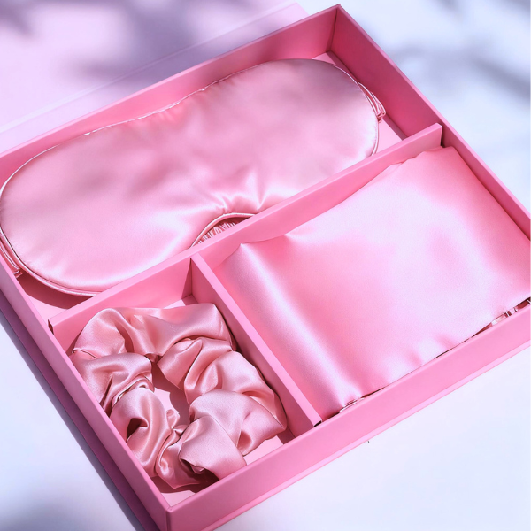 Pink luxury satin gift box with eye mask, scrunchie, and pillowcase for self-care.