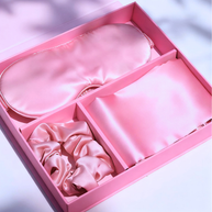 Pink luxury satin gift box with eye mask, scrunchie, and pillowcase for self-care.