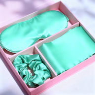 Mint green satin pillowcase, eye mask, and hair scrunchie in a pink gift box with ribbon.