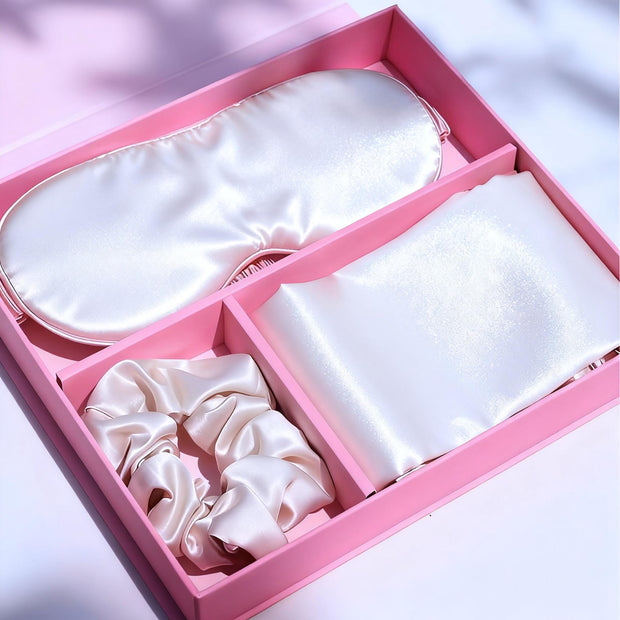White luxury satin pillowcase, eye mask, and hair scrunchie gift set in a pink box.