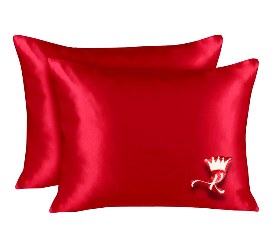 Two vibrant red satin pillowcases, one with a white crown and script 